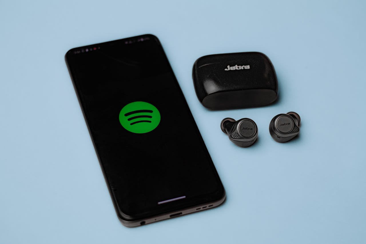 Closeup of Jabra true wireless earbuds with a smartphone displaying the Spotify app on a blue background.